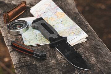 Travel essentials knife, compass, harmonica, map on a wooden table.