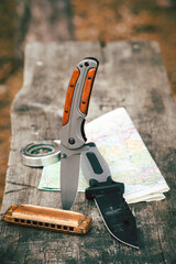 Knife with harmonica, compass and map wooden background.