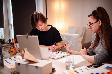 Two artists engage in a collaborative discussion over a watercolor palette, with one offering...