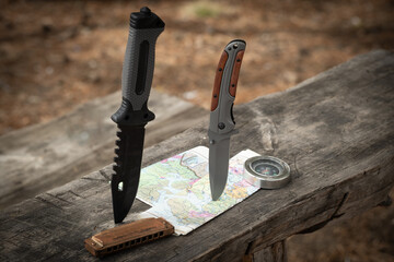 Hunting knife, compass and map on a wooden table in the forest. Concept of adventure.