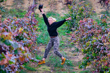 Joyful mature young blondy farmer woman jumping in a vineyard farmland.