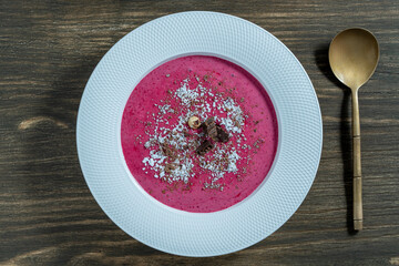 Sweet summer cherry soup in a white plate on a wooden background, closeup, top view. Hungarian cold red cherry soup with yogurt or cream, sprinkled with grated chocolate, powdered sugar and hazelnuts - 788711765