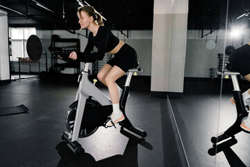 A woman gives her all on a stationary bike at the gym, her focused expression mirroring the effort of her intense cardio session.