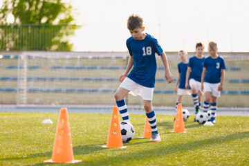 Happy Boys on Soccer Training Slalom Drill. School Kids Practicing European Soccer on the Grass School Field. Soccer Training - Warm Up and Slalom Drills - obrazy, fototapety, plakaty