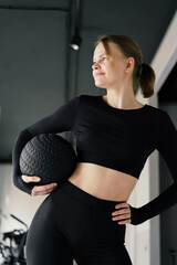 A poised athlete cradles a medicine ball at her hip, her gaze distant and contemplative, amidst a...