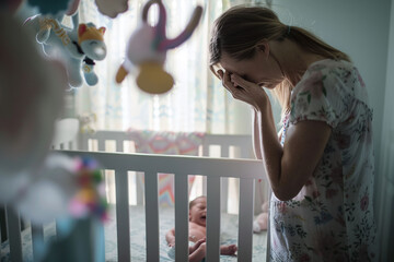 Distressed mother by baby's crib, postpartum depression concept. Design for healthcare, poster, support group
