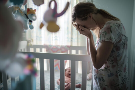 Distressed mother by baby's crib, postpartum depression concept. Design for healthcare, poster, support group