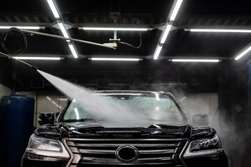 A man washes foam off a black car with water at a car wash.