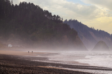 Couple walking along a misty beach on a beautiful colorful morning. Oregon beach walking at dawn on a springtime day with a rugged coastline in the background.