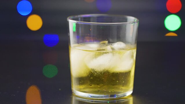 Closeup of a glass of whiskey with ice on a bar table and being shaken