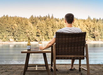 Young man enjoying a peaceful moment outdoors in nature relaxing with glass of wine and book 