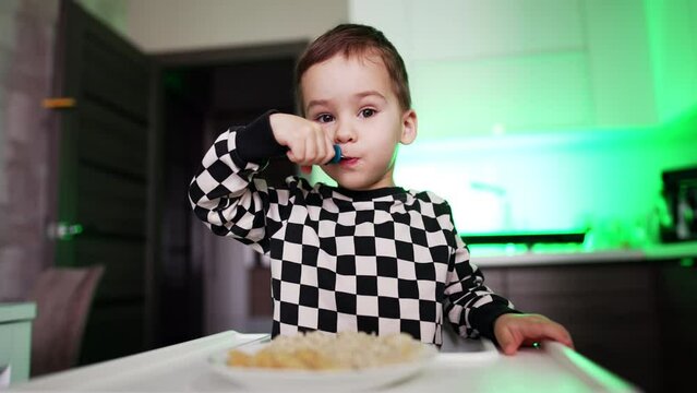 Lovely boy wearing checkered shirt eats from a fork. Two-year-old toddler eating himself. Low angle view.