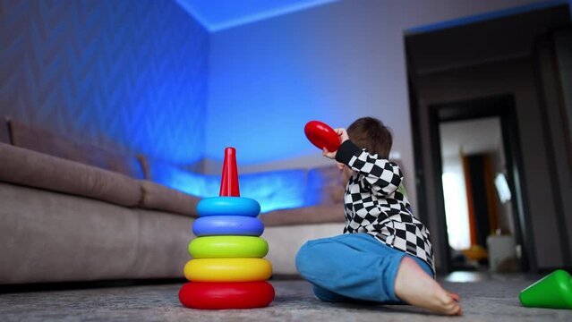 Toddler kid sits in the room busy with a game. Baby boy building a colorful pyramid. Low angle view.