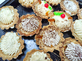 Assortment of Cream Topped Tarts in a Display Case. Rows of freshly baked tarts topped with cream and garnishes