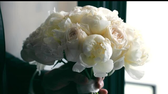 A bouquet of white peonies with roses in hands. The groom is holding a bouquet for the bride, a wedding bouquet. The concept of floristry and wedding decoration.