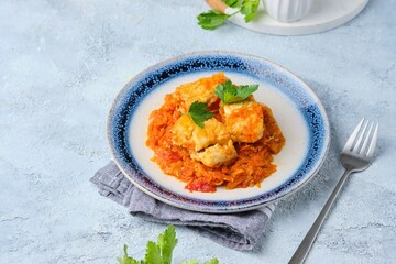 Cold appetizer, Christmas fish in a sauce with carrots, onions and tomatoes in a Polish style on a ceramic plate on a light concrete background.