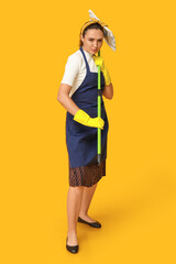 Portrait of focused young housewife in apron with mop on yellow background