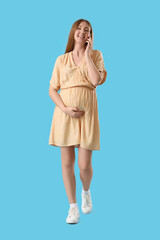 Young pregnant woman talking by mobile phone on blue background
