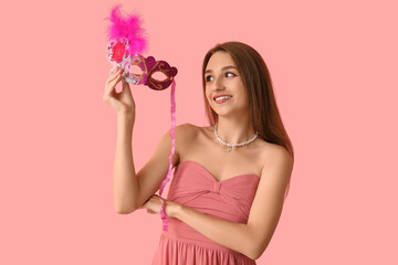 Beautiful young woman with carnival mask on pink background