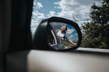 A happy, carefree woman with her hair blowing in the wind, reflected in a vehicle's side mirror during a scenic road trip.