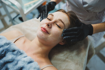 Medicine and cosmetology. The hands of a beautician in black gloves are massaging the face....