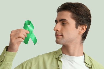 Young man with green ribbon on light background, closeup. Glaucoma awareness month