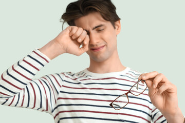 Tired young man with eyeglasses on light background, closeup. Glaucoma awareness month