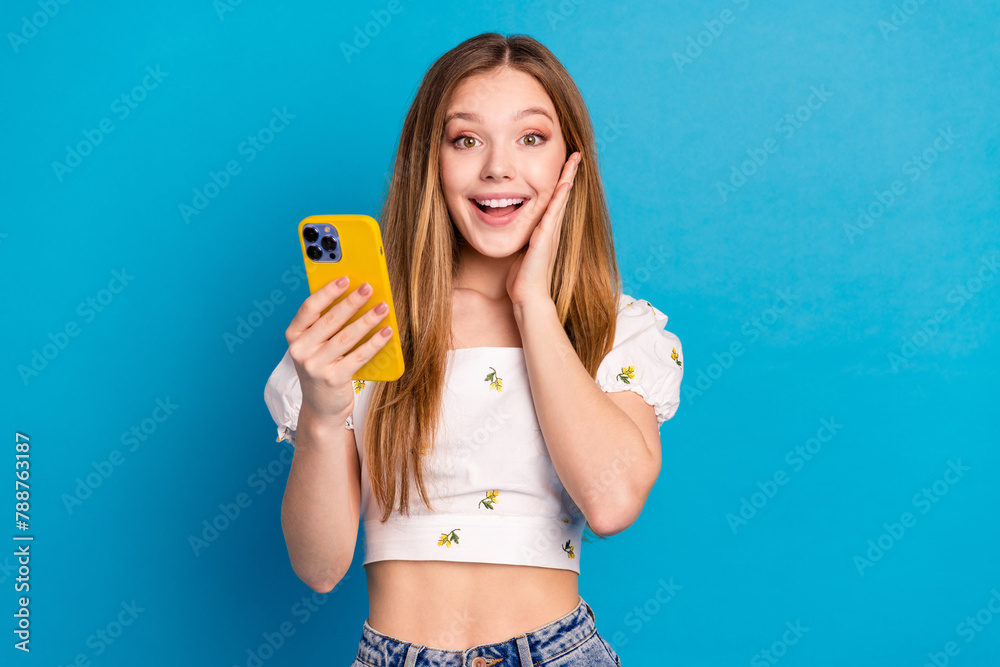 Poster Photo of surprised girl using cell smart gadget isolated blue color background