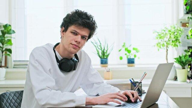 Young male college student sitting at desk with laptop looking at camera