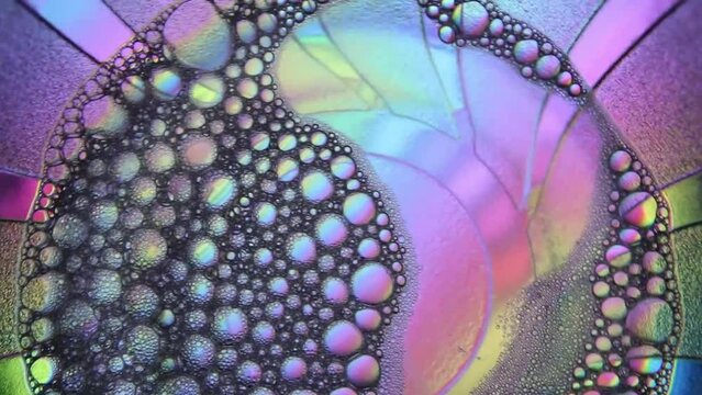 Esferas de burbujas flotando en la superficie colorida de un cuenco labrado con curvas y ondas, con movimiento de giro lento se juntan y refractan la luz multicolor del fondo en bokeh  