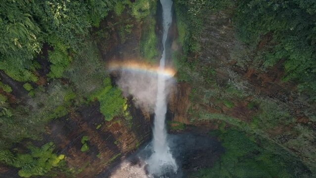 Aerial view fly orbiting over Kapas Biru Waterfall with rainbow, Java, Indonesia