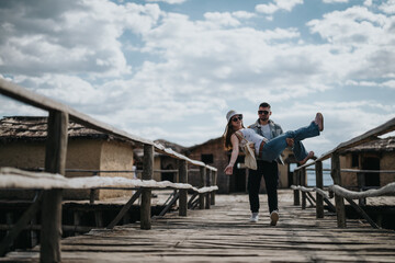 A happy couple shares a carefree, joyful moment as they walk along a wooden pier during their...