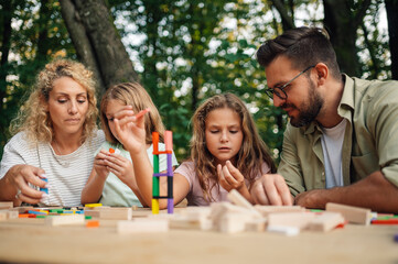 A young family is playing wooden blocks game at picnic table in nature