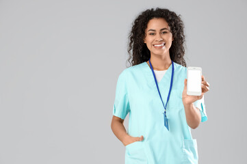 Female African-American medical intern with mobile phone on light background
