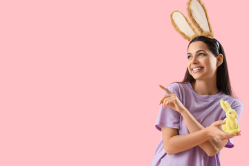 Young woman in bunny ears with Easter rabbit pointing at something on pink background