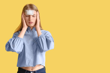 Young woman with brain concussion and medical patch on yellow background