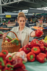 Young woman with basket purchasing peppers at food market.