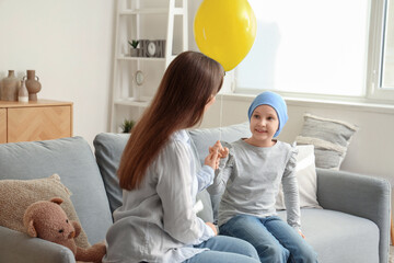 Little girl after chemotherapy with blue balloon and her mother at home. International Childhood...