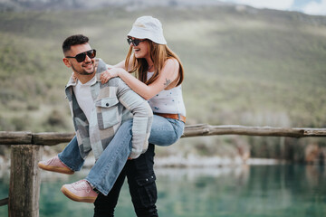 A happy couple sitting on a wooden fence shares a laugh against a stunning lake backdrop, embodying the joy of travel.