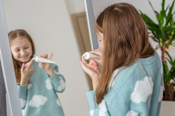 Child Smiling Applying Facial Cream in Mirror. Morning preparation before school.