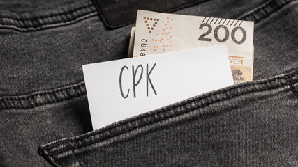 White card with a handwritten inscription "CPK", inserted into the pocket of gray pants jeasnow, next to Polish banknotes PLN (selective focus)