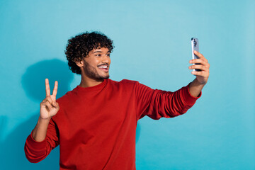 Photo of friendly latin guy with curls hairstyle in red pullover make v sign photographing selfie...