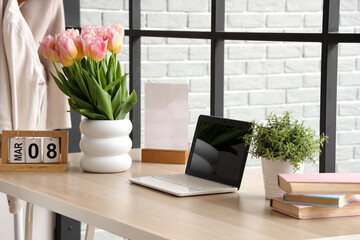 Calendar with date of International Women's Day, tulips and laptop on table in room