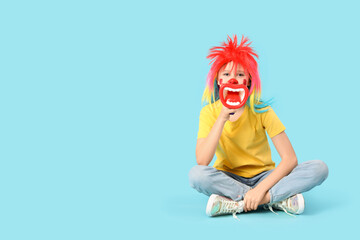 Funny girl in clown costume with megaphone on blue background. April Fool's Day celebration