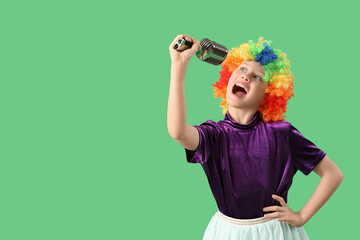 Funny girl in clown costume with microphone on green background. April Fool's Day celebration