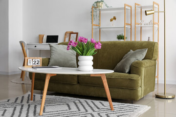 Vase with tulips, magazine and calendar on table in stylish living room interior
