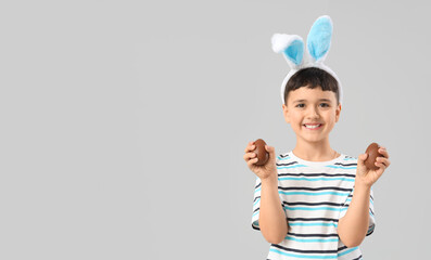 Cute little boy in bunny ears headband with chocolate eggs for Easter on white background
