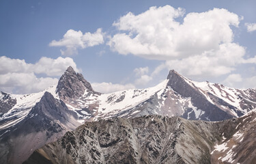 Panoramic landscape in the mountains with rocks and scree, with grass glades, snow and glaciers on a sunny summer day in the Fann Mountains in Tajikistan with mountain ranges