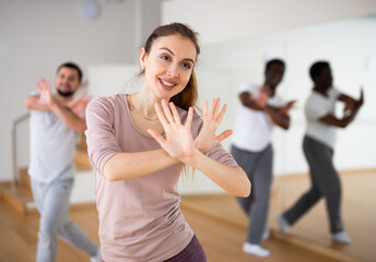 Portrait of cheerful young woman enjoying active dancing during group training in dance studio..