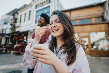 Happy young woman enjoying ice cream with a smiling man behind her in a casual urban setting.